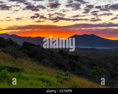 Dramatic sunset, Sky on fire as sunsets behind hills. Majestic, a kaleidoscope of colours glowing with the last sunlight, winter, Australia Stock Photo