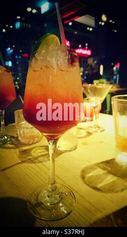 A photograph of a colourful cocktail drink surrounded by other glasses and drinks on a table in a bar. Alcohol, socialising, drinking in a pub concept. Stock Photo