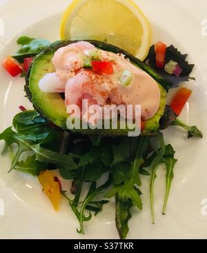Avocado filed with fresh pink prawns, Marie Rose sauce and salad with a lemon slice on a white plate Stock Photo