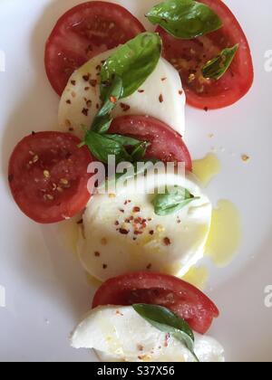 Flat lay of a salad consisting of mozzarella cheese slices, vine ripened tomatoes, fresh basil leaves and spiced olive oil Stock Photo