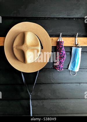 Straw hat and 2 face masks hanging on hooks by door in mud room Stock Photo