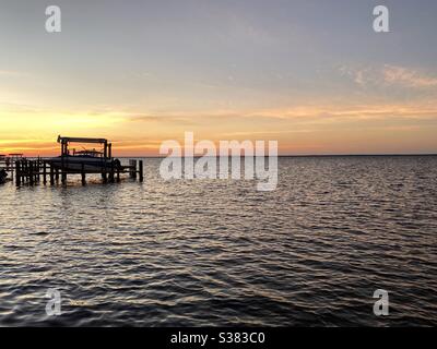 Bright colorful sunset skies over bay water with boat dock Stock Photo