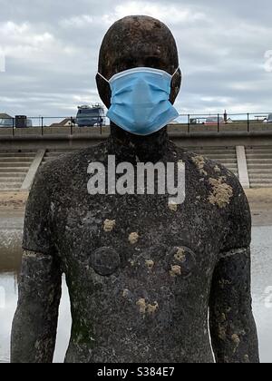 Antony Gormley’s Another Place on Crosby beach, Liverpool, where one of the life-sized metal statues has been decorated by a face mask and in a reference to the coronavirus. Stock Photo