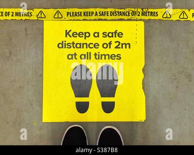 Two feet alongside a sign on the floor of a store instructing shoppers to maintain social distancing. Stock Photo