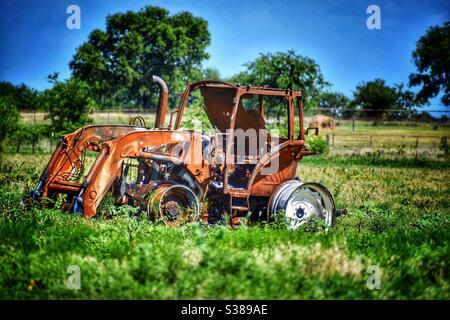 Old burned and rusted tractor sitting in the hot sun in a green country field. Stock Photo