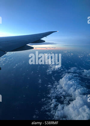 A view of the sky at sunrise from an airplane window showing some clouds and the airplane wing. Stock Photo