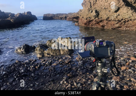 Canon EOS R camera on tripod making a seascape photograph with filters in a rocky cove on the coast of Tenerife Canary Islands Spain Stock Photo