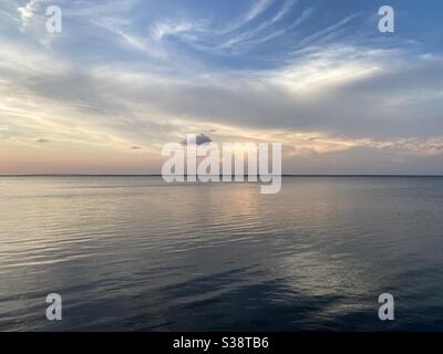 Sun reflecting into soft white fluffy clouds over bay water at sunset Stock Photo