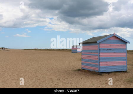 Great Yarmouth beach cabins in a summer day, traditional UK cabin on an English East Coast, blue and pink horizontal stripes, sky with clouds no people, large stretch of sand, UK beaches Stock Photo
