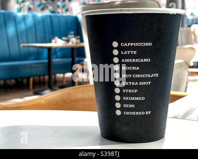 Disposable coffee cup on a table with list of coffees and options. No people. Stock Photo