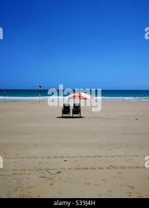 Two deckchairs under an umbrella on empty beach Stock Photo