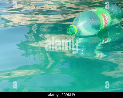 Bright green empty plastic bottle of crown floating on reflective waves Stock Photo