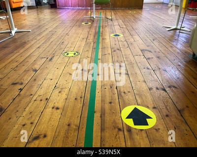 Markings on a wooden hall floor mark out a one way system as a consequence of social distancing due to coronavirus. Stock Photo