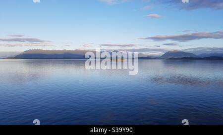 Sea landscape, sunset over hillside, blue sky with clouds reflecting in the water Stock Photo