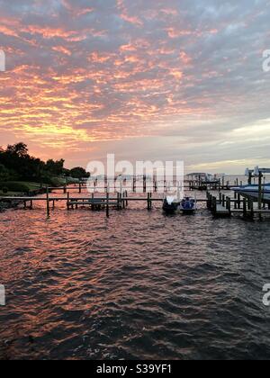 Colorful sunset skies over bay water with boat dock and reflections on ...