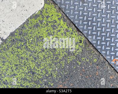 Grunge texture background with green paint on asphalt surface next to patterned metal and concrete Stock Photo