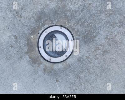 Detail of light with textured glass cover, embedded in concrete sidewalk, creating abstract background texture Stock Photo