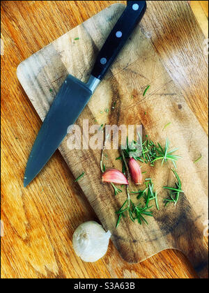 An overhead view of a chopping board with Rosemary, Garlic and a kitchen knife. Flavours are being prepared! Photo Credit - ©️ COLIN HOSKINS. Stock Photo