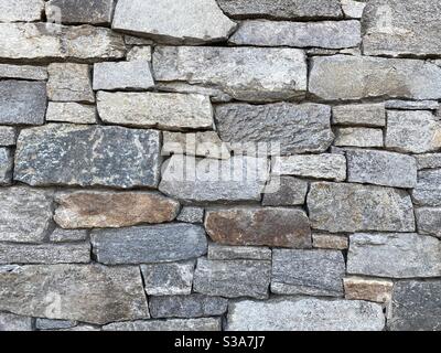 Close view of wall of oddly shaped, grey and other earth-tone bricks made of rock, creating abstract background texture suitable for compositing Stock Photo