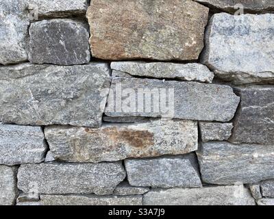 Detail of oddly shaped, grey and other earth-tone bricks in a wall made of rock, creating abstract background texture suitable for compositing Stock Photo