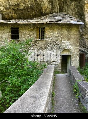The old stone bridge on the Dora of Verney stream with an abandoned house built in the rock of the mountain, Pre’-Saint-Didier, Aosta, Italy Stock Photo