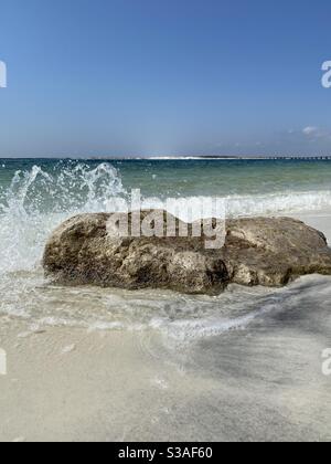 Waves crashing against large rocks in the sand on the beach Stock Photo