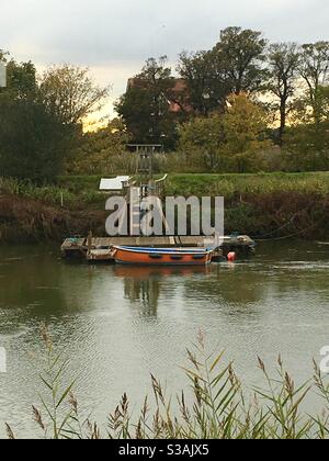 Small Orange rowing boat moored on river next to wooden jetty Stock Photo