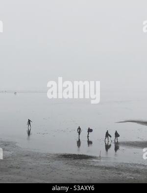 Silhouettes of surfers on a cold, wet beach, Westward Ho, Devon, UK Stock Photo
