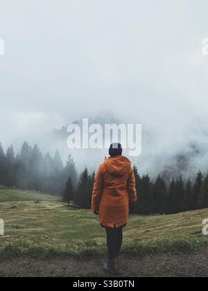 The back of a woman in a yellow jacket looking at a Misty Valley in the German alps, Bolsterlang, Germany Stock Photo