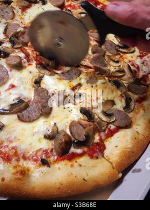 Close up of a metal pizza wheel cutting a mushroom and sausage pizza, USA Stock Photo