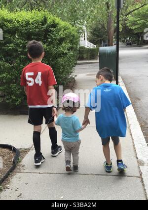 2 young brothers walking their Toddler girl cousin outdoors from behind. Stock Photo
