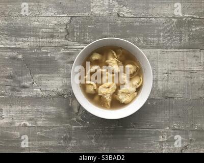 A bowl of cappelletti meat filled pasta in chicken broth on a wooden background Stock Photo