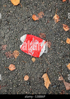 An overhead picture of a squashed Coca-Cola can. Discarded litter, thrown onto a tarmac path. Dead, Brown leaves means it’s autumn. Photo Credit - ©️ COLIN HOSKINS. Stock Photo