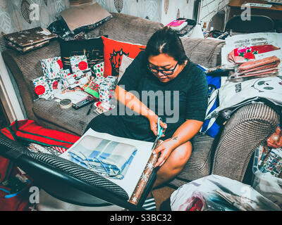 A lady wraps Christmas presents sat on a sofa. Stock Photo