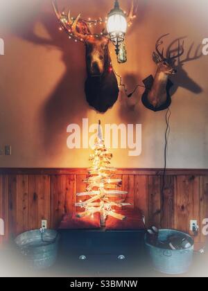 Driftwood Christmas tree decorated with white lights underneath moose and deer heads Stock Photo