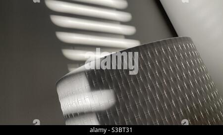 Abstract background pattern of light and shade with sunlight from blinds falling on textured lampshade and wall Stock Photo
