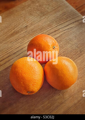 A group of three enticing oranges lye on a wooden table top. A simple but graphic image. Room for copy. Photo Credit - ©️ COLIN HOSKINS. Stock Photo