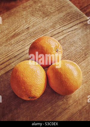 An atmospheric image of three oranges clumped together on a wooden table top. Space for copy. Graphic shapes. Photo Credit - ©️ COLIN HOSKINS. Stock Photo
