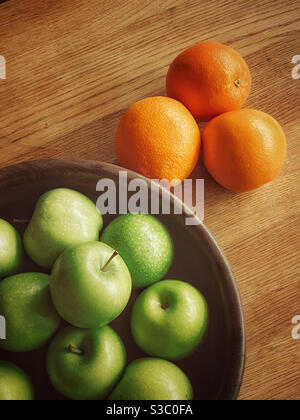 A wooden fruit bowl filled with Green Granny Smith Apples & next to a group of 3 oranges. Fruit means healthy eating & a balanced diet. Photo Credit - ©️ COLIN HOSKINS. Stock Photo