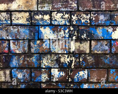 Old brick wall with faded peeling layers of ancient painted graffiti. Stock Photo