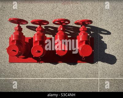Bright red fire extinguisher connectors and taps on the outside of a stone-tiled building. Used by fire fighters to connect hoses during an emergency Stock Photo