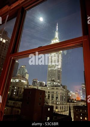 A room with a view! A beautiful view of the lit up Empire State building and the full moon on a winters night in Midtown Manhattan, New York, USA Stock Photo