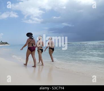 Three women walking along the shoreline at at beach in Mexico. They are all wearing bikinis & sun hats Stock Photo