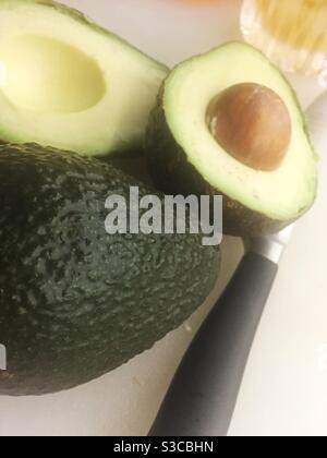 Two avocados on a cutting board with a knife Stock Photo