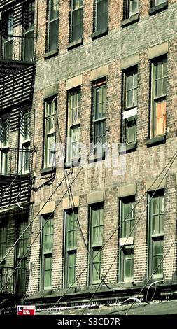 Gritty, poor, deprived neighbourhood in Manhattan New York City USA. A brick building of flats and apartments with metal fire escape with smashed and boarded up windows in NYC Stock Photo