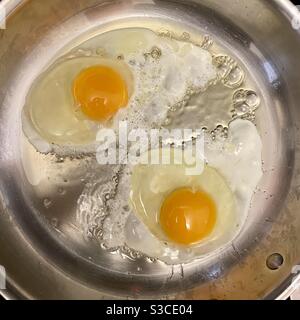 Overhead view of two eggs cooking in a stainless steel frying pan Stock Photo