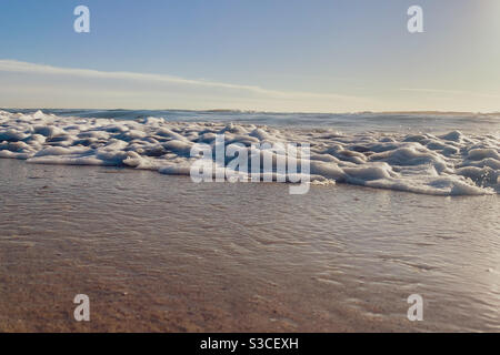 A gentle wave rolling onto sandy beach on a clear day Stock Photo