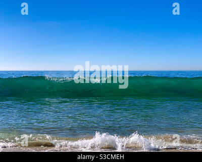 Ocean waves breaking onto sandy beach on a sunny day. Stock Photo
