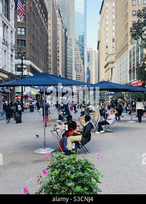 A painter leaving yet of New York City life on the sidewalks of Herald Square in Midtown Manhattan as people stroll or sit under blue umbrellas surrounded by skyscrapers on a quiet afternoon Stock Photo