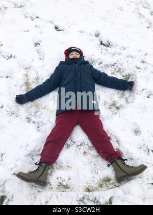 A child lying down on the floor in snow making a snow angel. Stock Photo